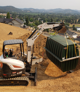 Crane lowering a concrete septic tank onto a truck bed